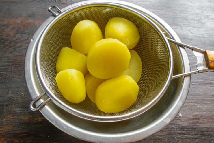 Boiled potatoes steaming in a metal colander to dry out.