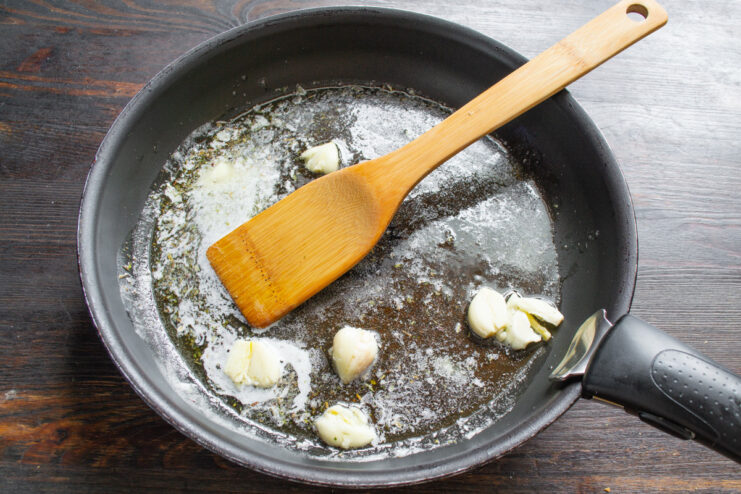Smashed garlic cloves sizzling in melted butter and olive oil in a skillet.