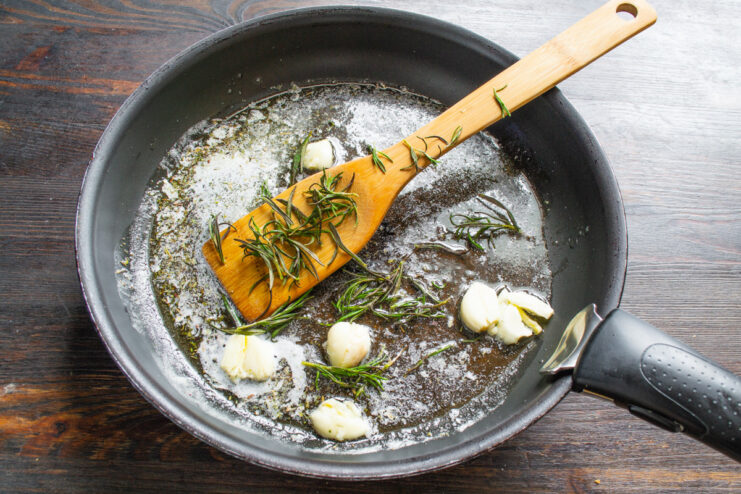 Fresh rosemary leaves being added to the skillet with garlic and oil.