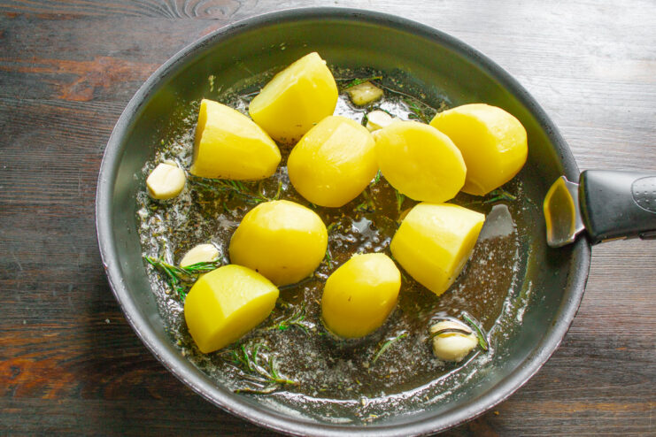 Boiled potatoes being added to the skillet with the rosemary and garlic oil.