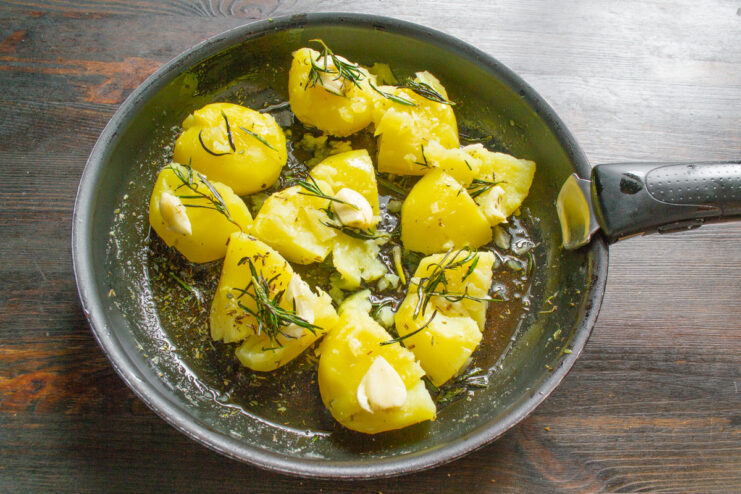 Using a potato masher to gently smash the boiled potatoes in the skillet.