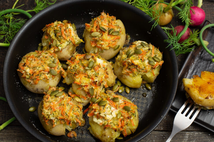 A dish of baked potatoes topped with a creamy cheese and vegetable mixture, garnished with pumpkin seeds.