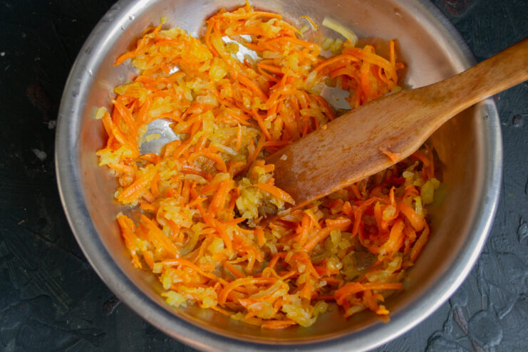 Cooking the Vegetable Base Until Tender Sautéed onions and grated carrots cooking in a skillet until soft.