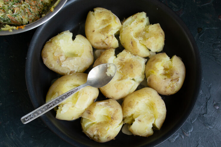 Smashing the Potatoes for a Crispy Texture Boiled potatoes in a skillet being gently smashed with a spatula.