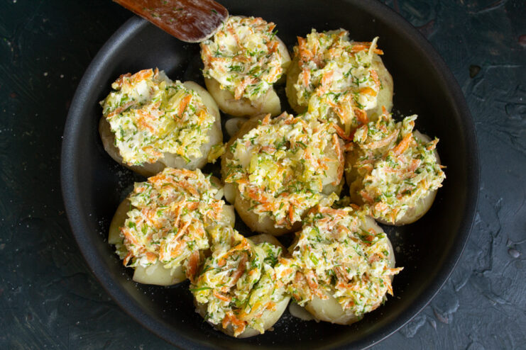 Topping the Potatoes with the Creamy Filling Smashed potatoes in a skillet being topped with mounds of the cream cheese and vegetable mixture.