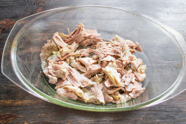 Assembling the Turkey and Potato Casserole Layering cooked turkey in a white casserole dish.