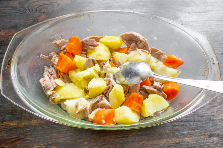 Mixing Turkey with Parboiled Vegetables Mixing cooked turkey with boiled potatoes and carrots in a casserole dish.