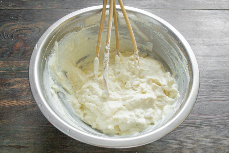 Adding flour to the batter to help bind the zapekanka. Adding a tablespoon of all-purpose flour to the cheese and egg batter in a bowl.