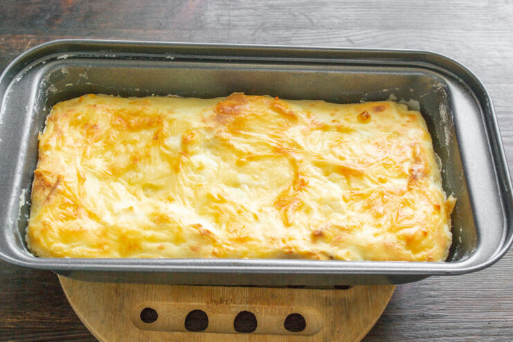 The freshly baked, golden-brown zapekanka cooling in its loaf pan. A perfectly baked, golden-brown Cheese and Lavash Zapekanka cooling in a loaf pan.