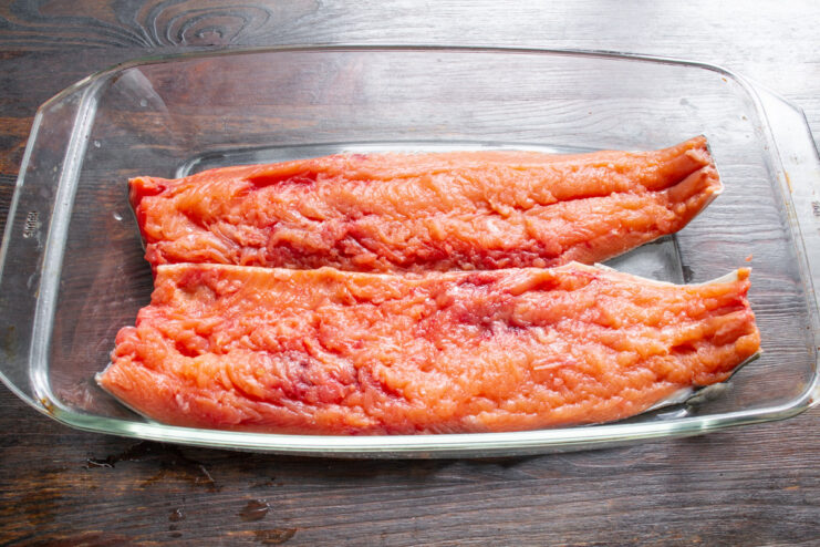 Placing Salmon Fillet in a Glass Dish for Curing A raw pink salmon fillet placed skin-down in a clear glass baking dish.