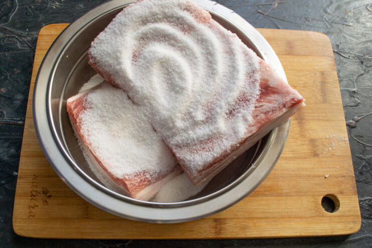 Seasoning the Salo with Salt and Sugar Cure Raw pork fatback being generously coated with a salt and sugar mixture in a bowl.