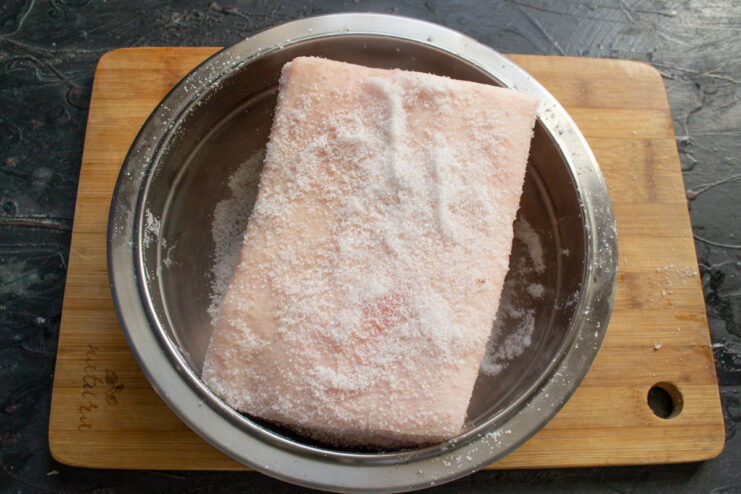 Properly Stacking Salo for Even Curing Pieces of seasoned pork fatback stacked skin-side out in a curing container.