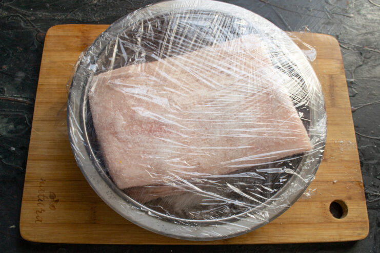 Covering the Salo to Begin the Curing Process A bowl containing seasoned salo covered tightly with plastic wrap.