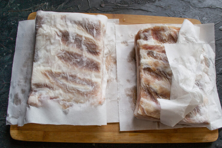 Drying the Cured Salo Before Adding Spices Cured pieces of salo being patted dry with paper towels on a wooden board.