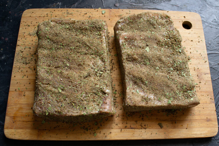 Applying the Final Spice Rub to the Cured Salo A hand rubbing a dark spice mixture onto a piece of cured and dried salo.