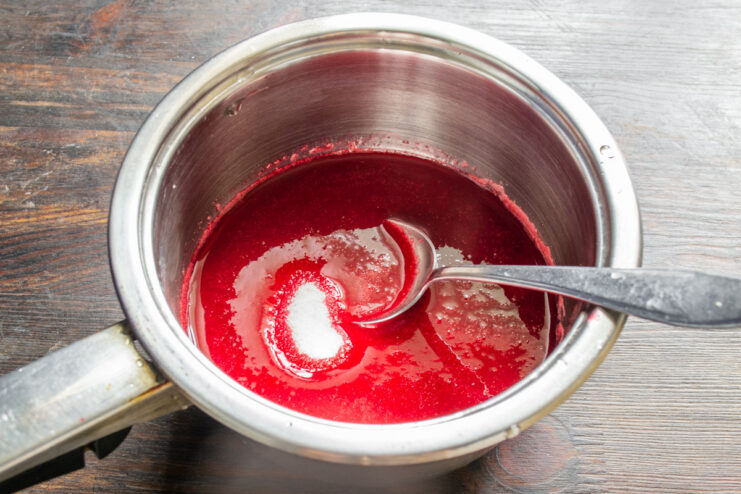 Cooking the raspberry puree with sugar A saucepan with pink raspberry puree and sugar being heated on a stove.