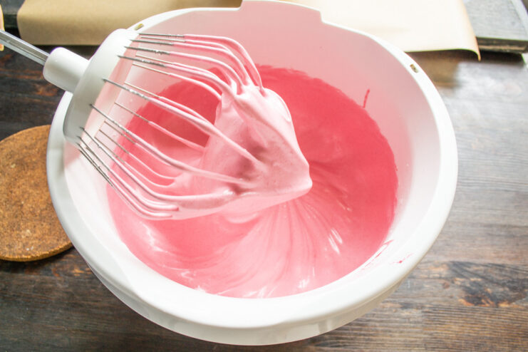 Whipping the raspberry puree and egg white into a meringue A stand mixer whipping raspberry puree and egg white into a fluffy pink meringue.