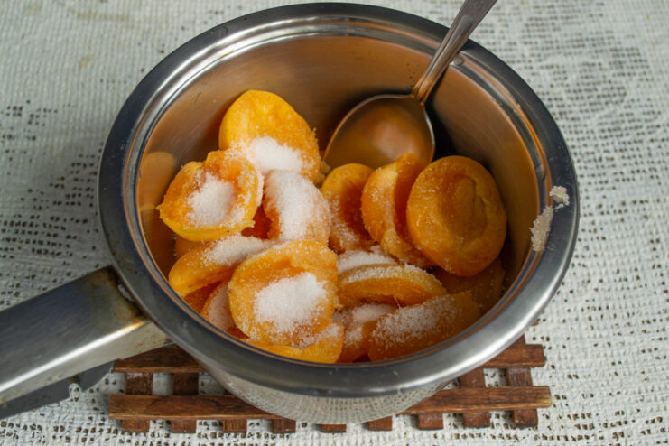 Adding sugar for maceration Apricot halves in a saucepan sprinkled evenly with granulated sugar.