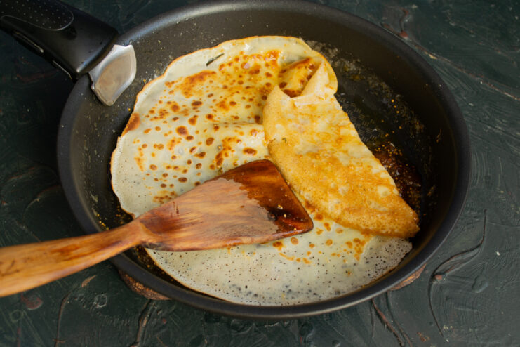 A crepe being folded in a skillet filled with fig sauce.