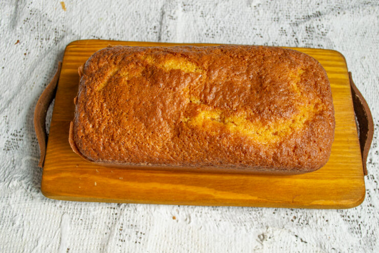 Cooling the Cake Whole baked cornmeal loaf resting on a wooden board.