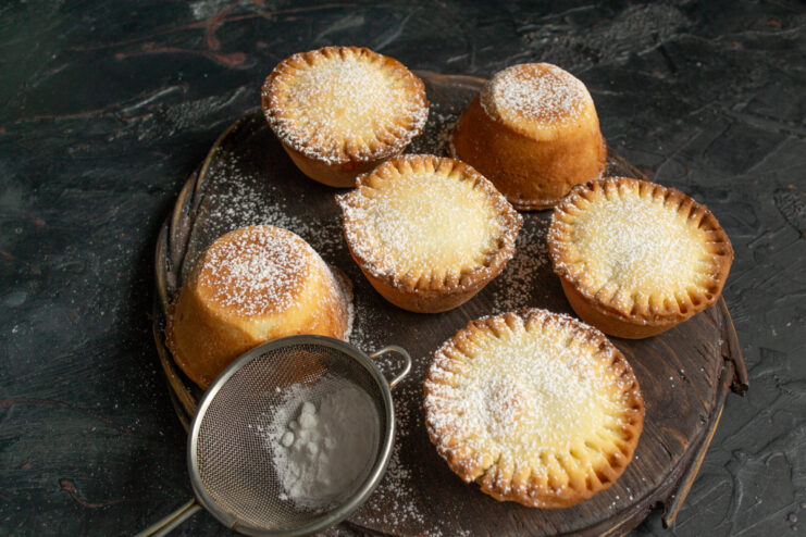 Dusting cooled tartlets with powdered sugar using a fine mesh sieve.