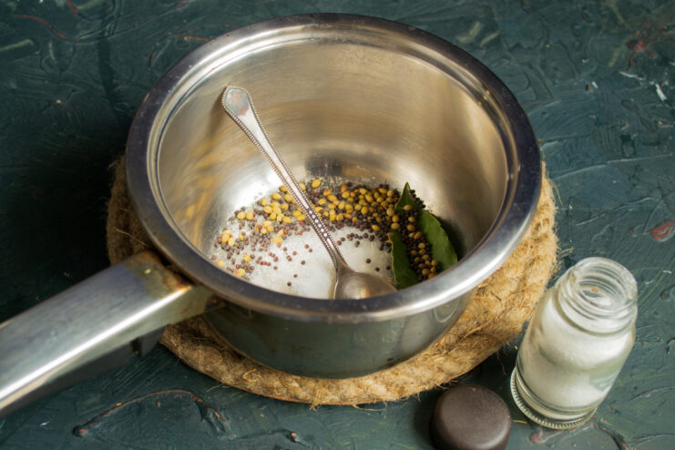Adding spices to the marinade Adding coriander, mustard seeds, and a bay leaf to the saucepan