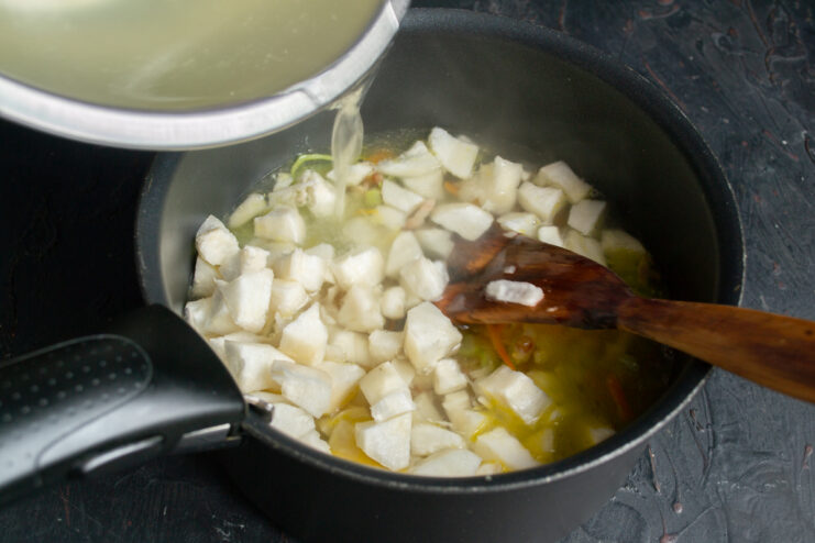 Pouring hot chicken broth over the vegetables Pouring hot chicken broth into the pot with sautéed vegetables