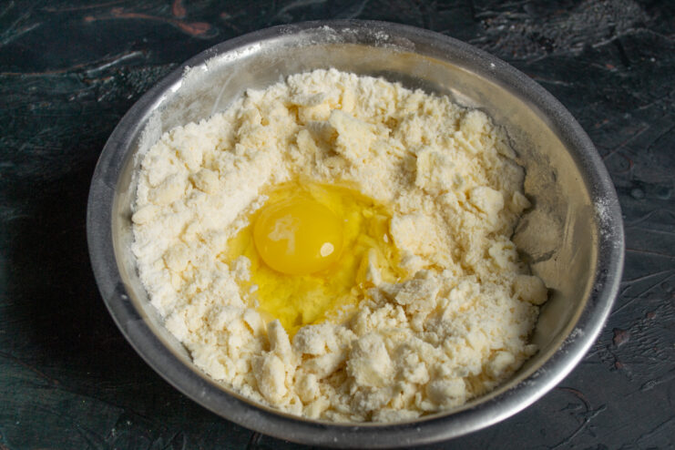 Adding a whole egg to the butter and flour crumb mixture in a bowl.