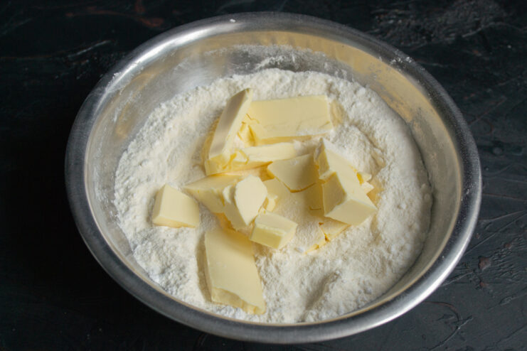Rubbing cold cubed butter into the flour mixture to create coarse crumbs.