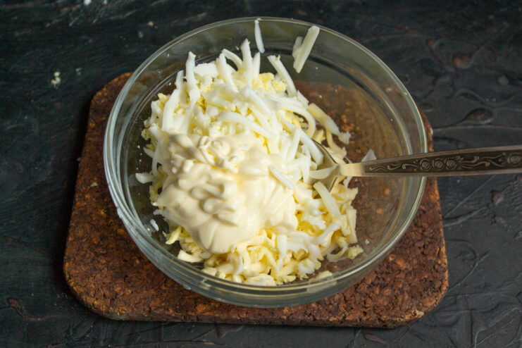 Adding mayonnaise and seasoning to the grated egg and cheese mixture