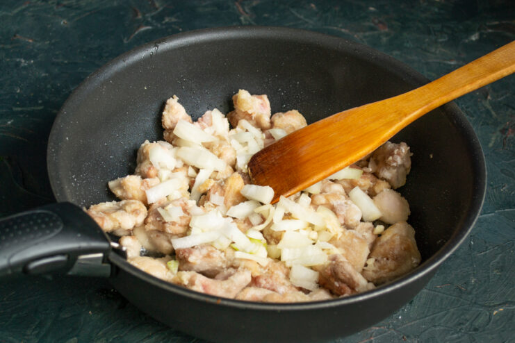 Adding Onion And Garlic Adding chopped onions to browned chicken in a pan