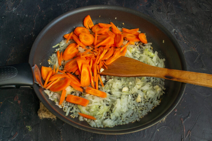 Adding carrots to the filling Adding julienned carrots to the sautéed onion in a skillet