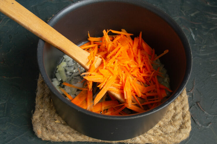 Adding carrots to the pot Julienned carrots added to sauteed onions in a pot.
