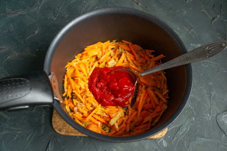 Building the Tomato Base Stirring rich tomato paste into sauteed vegetables in a pot.