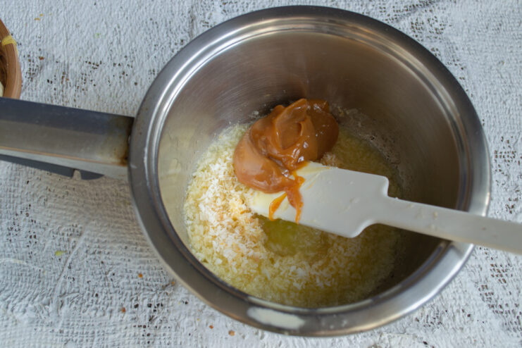 Adding boiled condensed milk Stirring boiled condensed milk into the coconut mixture in a saucepan