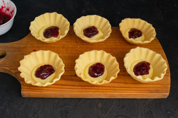 Adding the Jam Layer Spoonful of berry jam placed over buttercream inside a tartlet