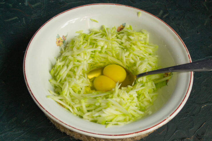 Mixing In The Egg Adding a raw egg with two yolks to the shredded zucchini