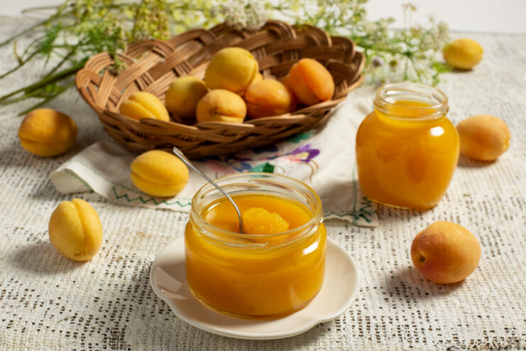 Homemade apricot marmalade in a glass jar alongside fresh fruits.