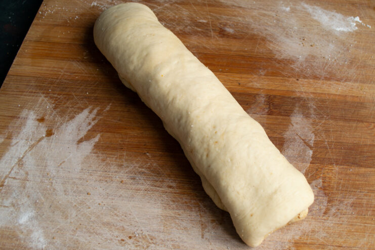 Shaping the roll Rolled yeast dough log sitting on a wooden cutting board