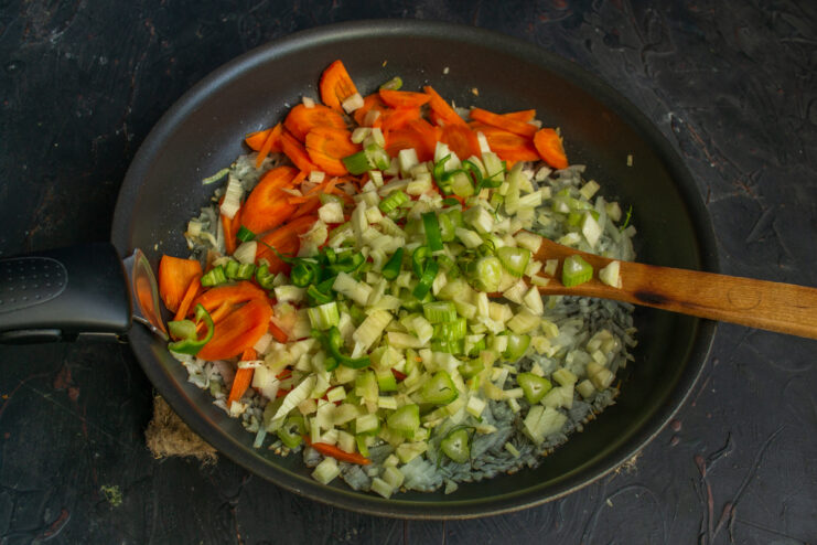Adding fennel and chili Adding chopped fennel and green chili to the vegetables in a skillet