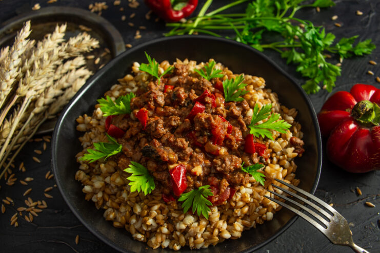 Cooked spelt topped with ground beef and vegetables garnished with fresh parsley.