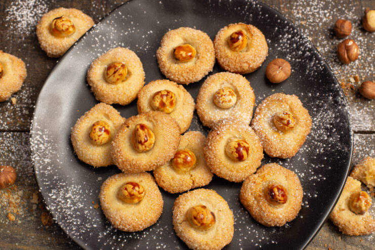 Baked hazelnut thumbprint cookies with whole nuts on a plate.