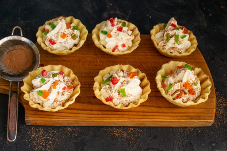 Final Decorative Touches Finished tartlets with whipped cream topped with candied fruits