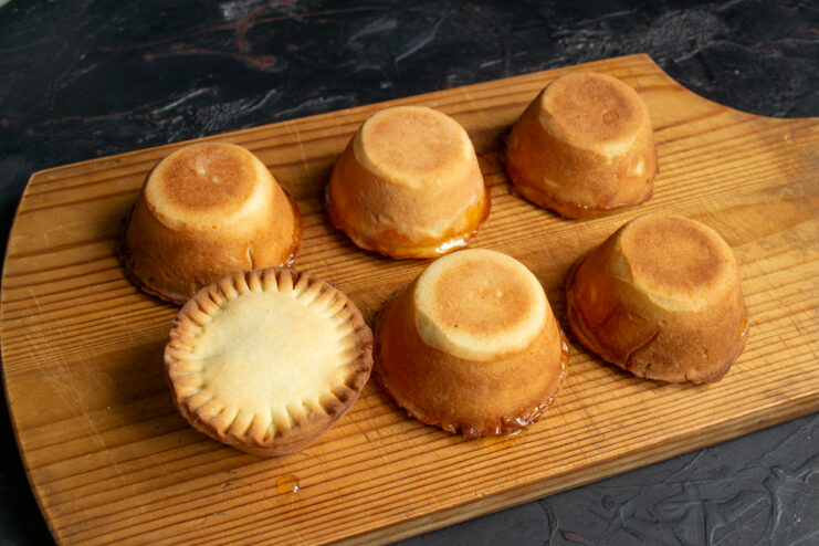 Baked tartlets cooling down on a wooden cutting board.