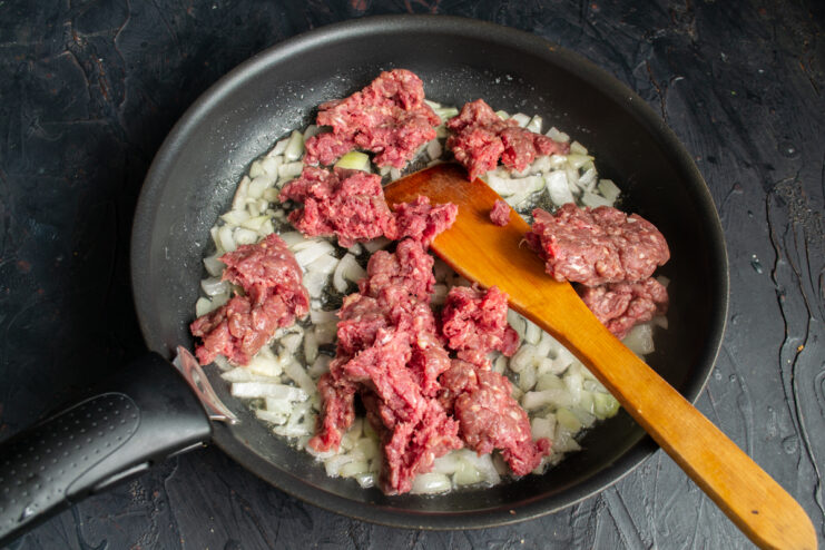 Adding the ground beef Raw ground beef added to sautéed onions in a frying pan.