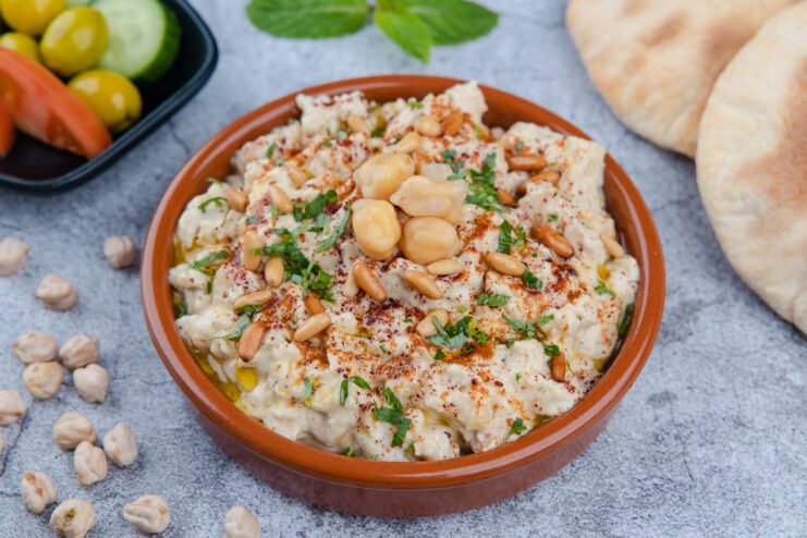 Light Hummus Topped With Pine Nuts Hummus beautifully garnished with toasted pine nuts, whole chickpeas, and paprika on a traditional plate.