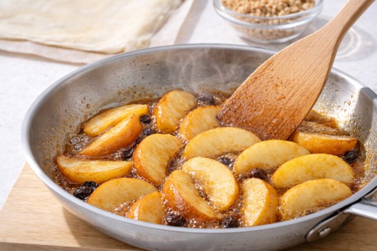 Caramelizing apples for strudel Apple slices caramelizing in a skillet with bubbling syrup and raisins next to a wooden spatula.