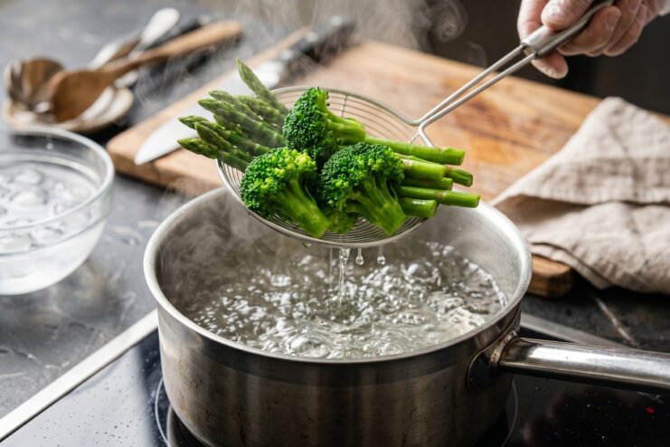 Removing broccoli and asparagus from boiling water using a slotted spoon