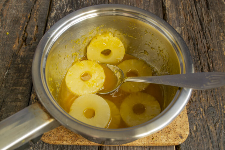 Cooking the Fruit Topping Pineapple rings simmering in orange syrup in a saucepan