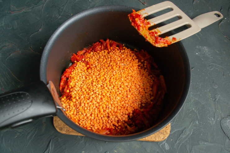 Adding the Red Lentils Dry red lentils poured over a seasoned vegetable base in a pot.